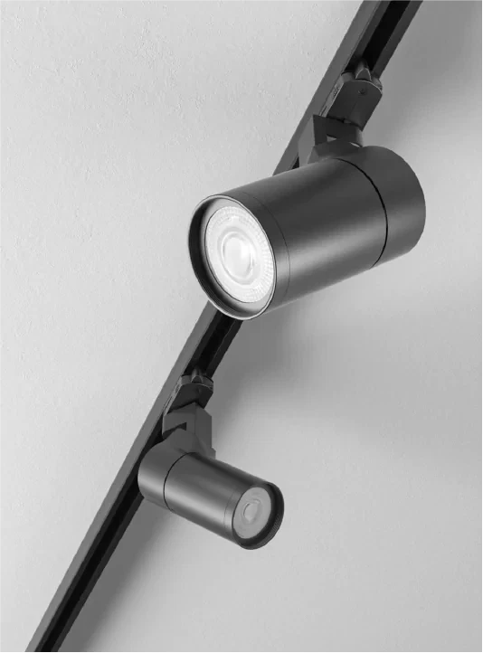 Black cylindrical LED track light with adjustable spotlight head mounted on ceiling rail